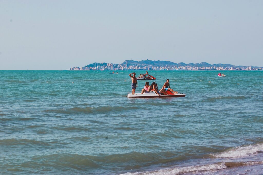 Menschen auf einem Tretboot im Meer vor der Küste von Durrës Albanien mit der Stadtansicht im Hintergrund.