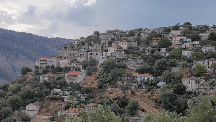 Entdecken Sie das malerische alte Qeparo-Dorf in Albanien, mit seinen wunderschönen Steinhäusern, die harmonisch in einen Hügel eingebettet sind.