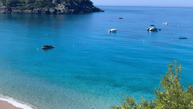 Strand von Jale Beach, Albanien. Kristallklares Wasser und Boote am Strand.